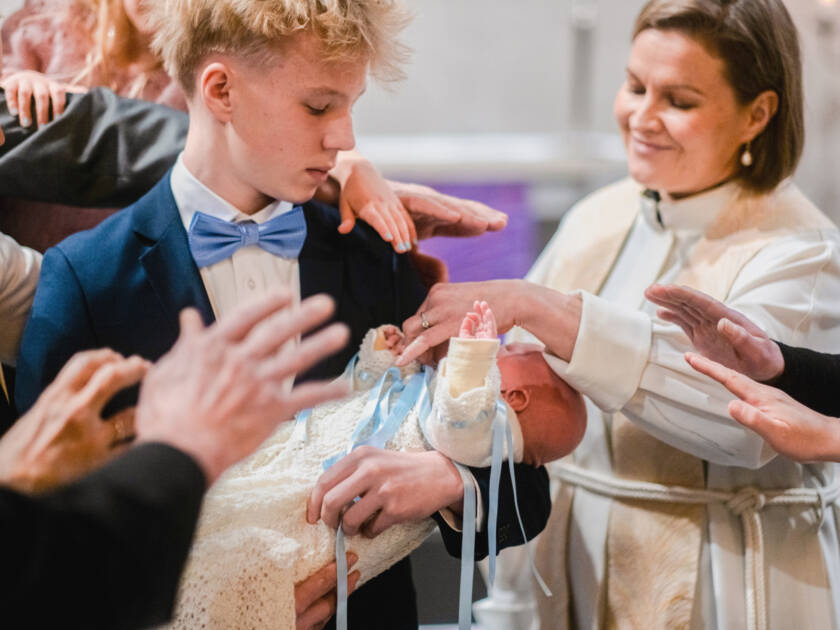 En präst och en grupp andra människor välsignar ett barn i dopkolt.