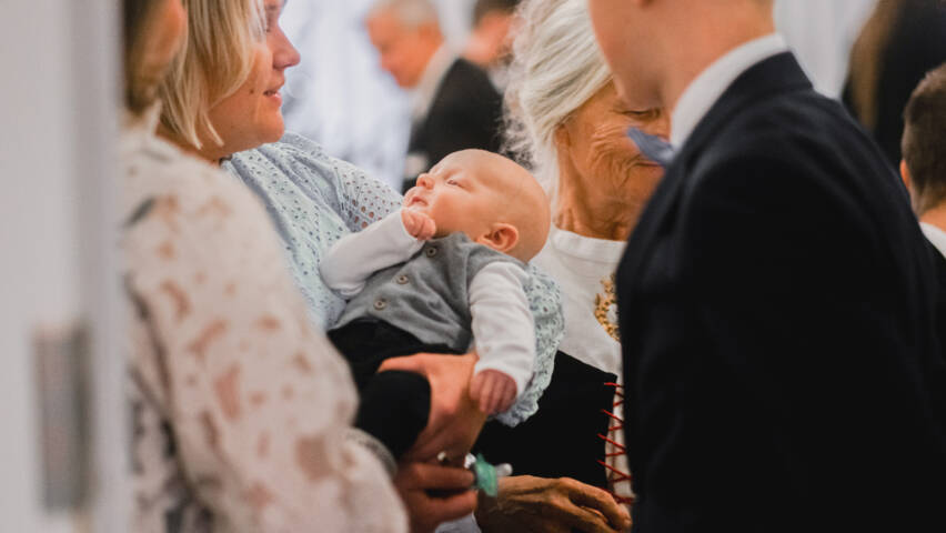 Personer på en dopfest. Babyn är i mittpunkten.