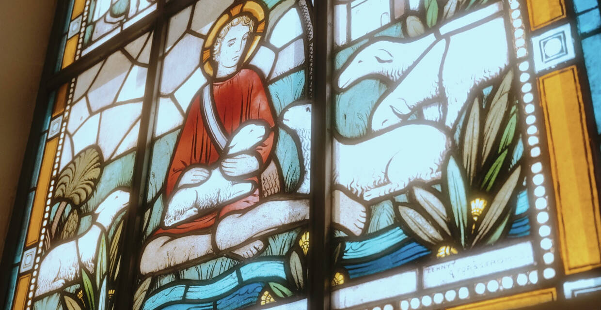 Ett färggrant glasfönster med Jesus och vita lamm.