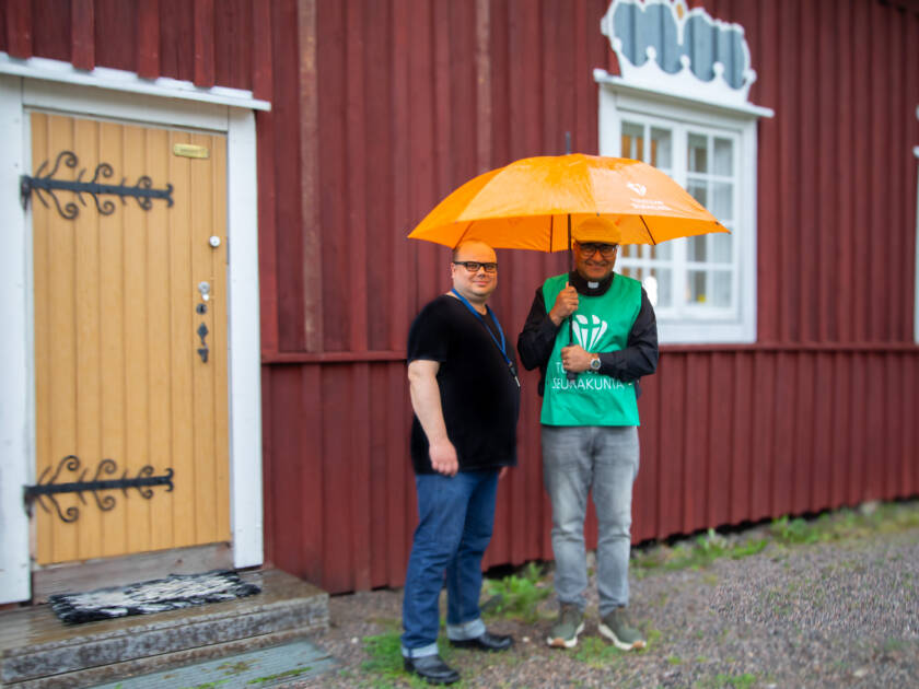 Työntekijöitä sateenvarjon alla Kellokosken kirkolla